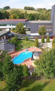 Luftaufnahme des Aparthotels am Rennsteig im Thüringer Wald mit Außenpool, Bäumen und Oßlaberg im Spätsommer
