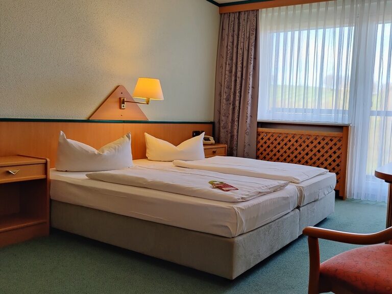 Helles Doppelzimmer im Aparthotel am Rennsteig mit großem Fenster, das einen Blick auf den grünen Thüringer Wald bietet.