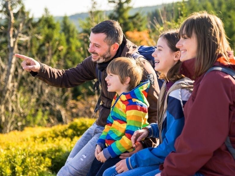 Eine Familie macht eine Pause im Wald, der Vater zeigt dem Sohn etwas in der Ferne.