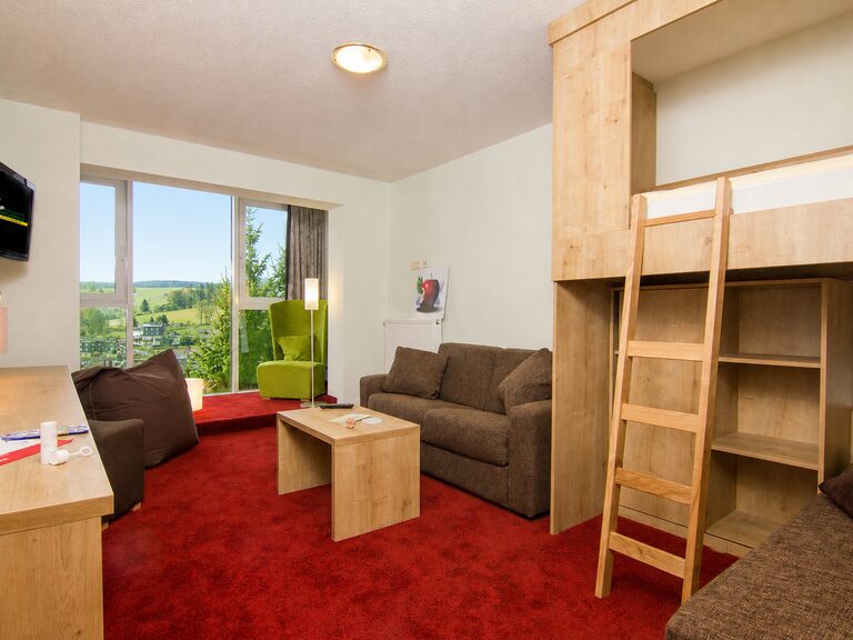 Familienurlaub Thüringen: Familienzimmer mit Panoramablick Familienzimmer mit bodentiefem Fenster und Balkon im Aparthotel Am Rennsteig. Ein idealer Rückzugsort für den Urlaub mit Kindern in Thüringen mit Blick in die Natur.