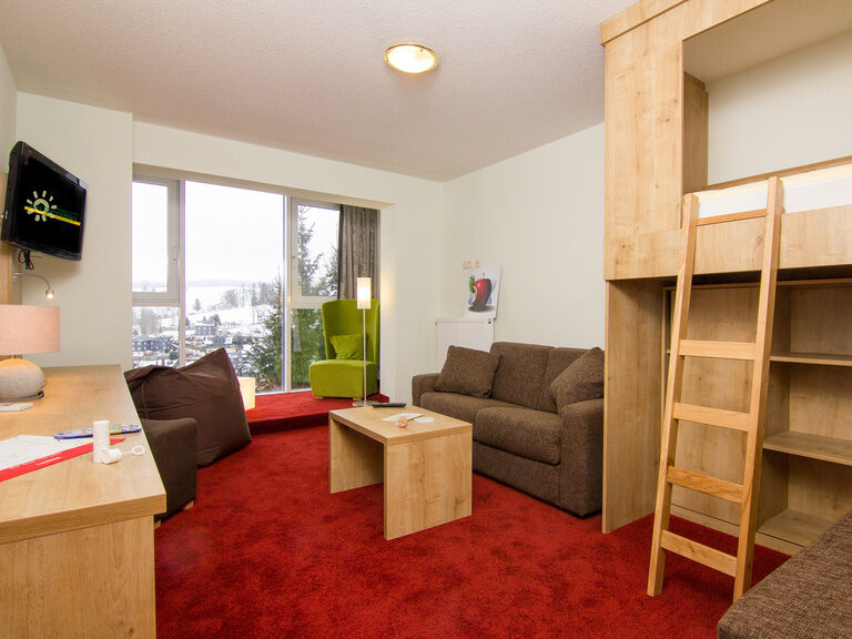 Kinderzimmer im Familienzimmer Superior mit rotem Teppichboden, Doppelstockbett und Blick aus dem Fenster in die Natur