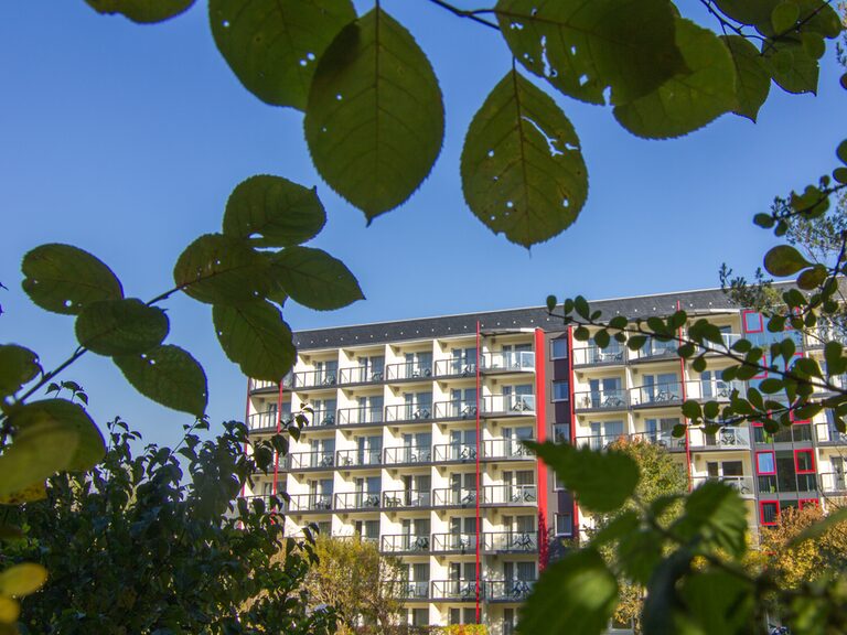 Blick durch buntes Herbstlaub auf das Aparthotel Am Rennsteig mit neuen Balkonen in der Abendsonne
