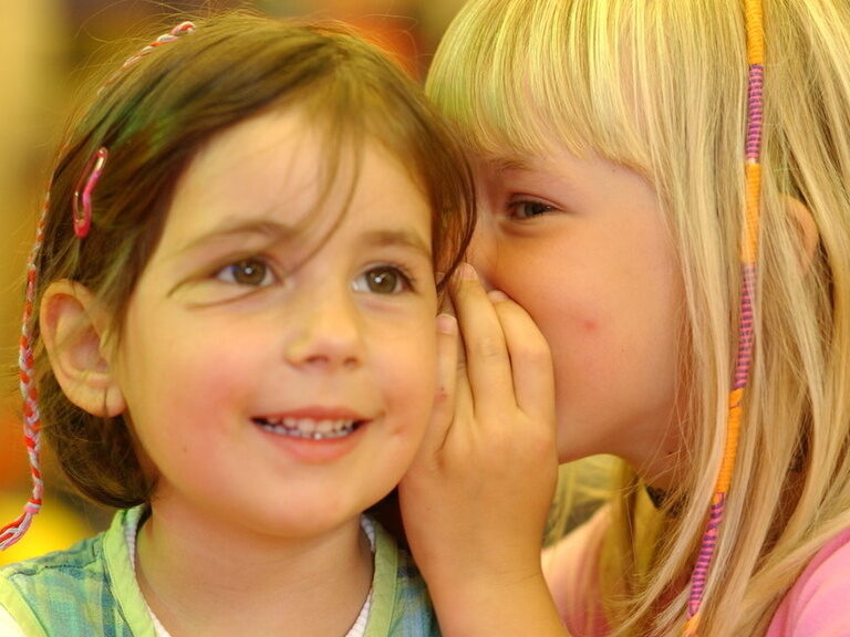 Kinderclub Familienhotel | Kinderanimation Thüringen Zwei Kinder flüstern sich im bunten Kinderclub des Familienhotels etwas ins Ohr, was die soziale Interaktion und die Geborgenheit zeigt.