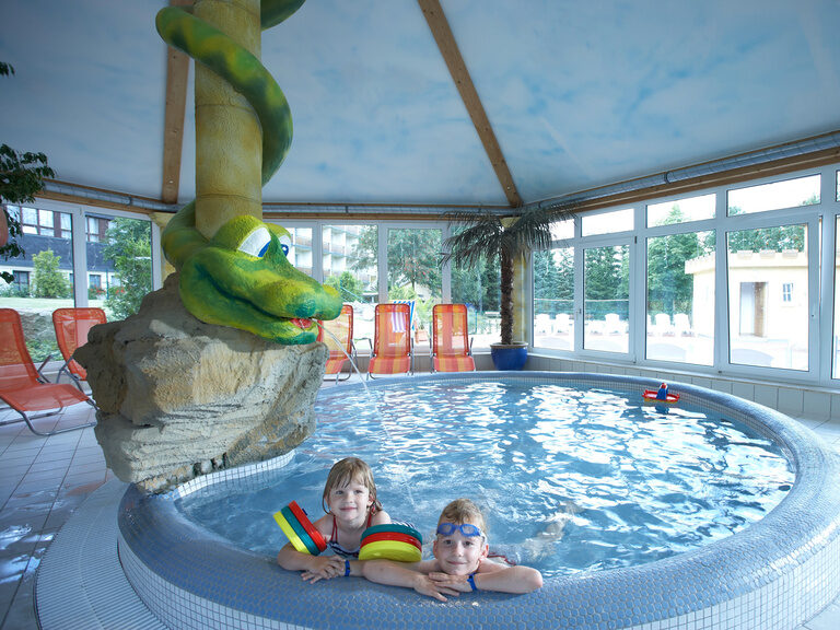 Kinder spielen vergnügt im flachen, bunten Kinderinnenpool des Familienhotels.