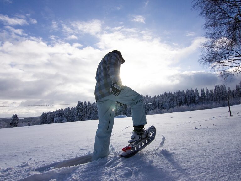 Eine Person geht mit im Hotel geliehenen Schneeschuhen durch den tiefen Schnee im Thüringer Wald. Zeigt das Wintererlebnis und den Service des Hotels.