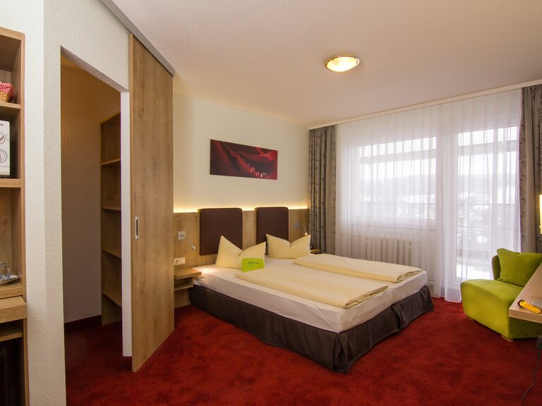 Superior-Elternzimmer im Aparthotel Am Rennsteig mit Doppelbett, Sessel und begehbarem Kleiderschrank, Blick in die Natur